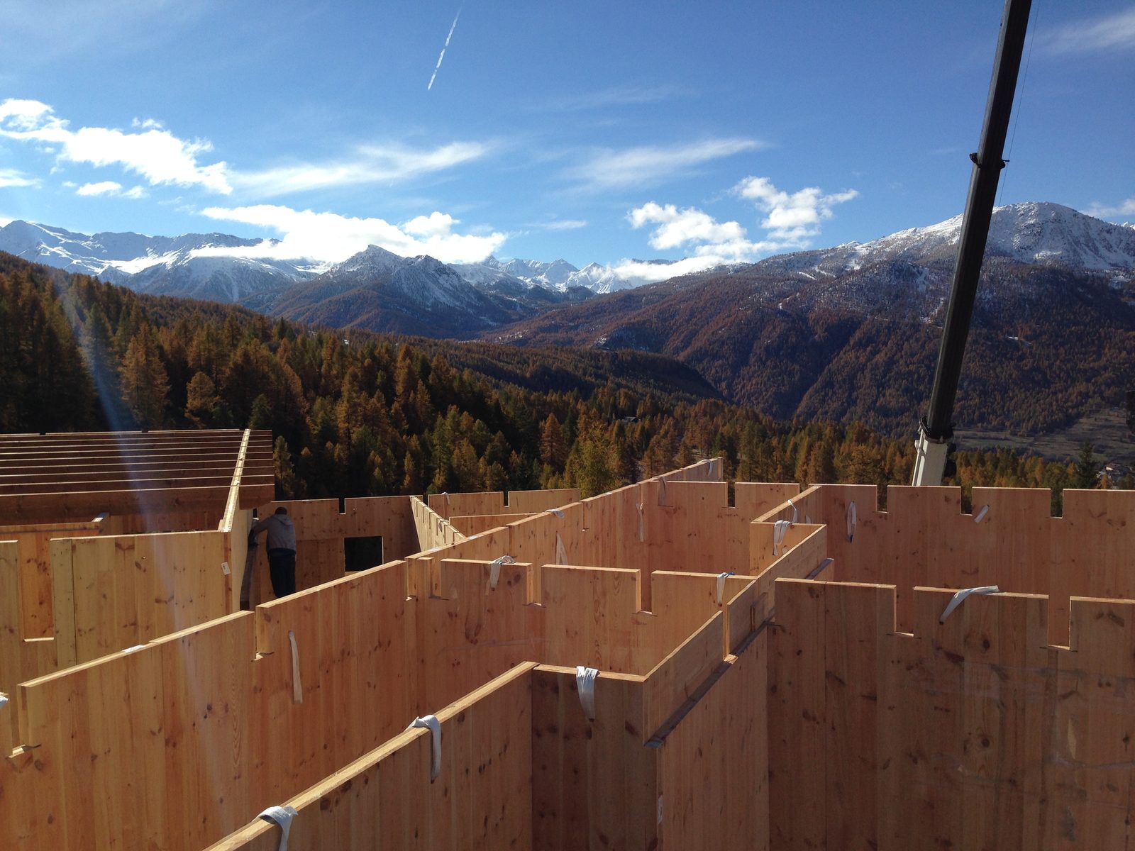 Cantiere in montagna: le pareti in pannelli X-Lam montate, la gru e i boschi di larici in autunno